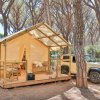 Una tenda da campeggio gialla con veranda in legno e un'auto vicina in una pineta.