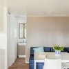 Interno con divano blu, tavolo bianco, piante in vaso, e angolo cottura. Sfondo chiaro.