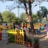 Area giochi colorata per bambini con staccionata, scivolo e altalene tra gli alberi.