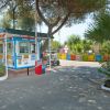 Ingresso con casetta di accoglienza e cartelli, circondato da piante e alberi.