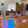 Due persone dietro un banco di accoglienza con volantini e scaffali sullo sfondo.