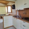 Cucina con mobili bianchi e piano cottura, lavello in acciaio, TV a parete e sedie in plastica.