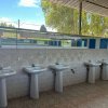 Un bagno all'aperto con file di lavandini bianchi su una parete piastrellata.