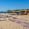 Spiaggia con lettini bianchi, ombrelloni blu e un chiosco in legno sotto un cielo limpido.