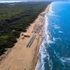 Spiaggia sabbiosa con ombrelloni, mare e vegetazione verde.