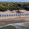 Vista aerea della spiaggia con ombrelloni blu e un chiosco, circondata da vegetazione.
