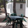 Tavolo con sedie verdi e roulotte bianche in un'area ombreggiata da alberi.