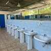 Diversi lavandini bianchi allineati in un bagno pubblico luminoso.