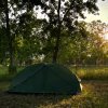 Tenda verde in un campo erboso, alberi intorno al tramonto.