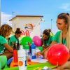 Persone sedute a un tavolo all'aperto con palloncini e materiali artistici.