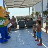 Un personaggio in costume giallo interagisce con bambini su una terrazza soleggiata.