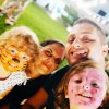 Una famiglia sorride, due bambini con il viso dipinto da tigre e coccinella.