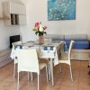 Sala da pranzo con tavolo apparecchiato, sedie bianche e quadro di fiori su sfondo blu.