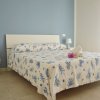 Camera con letto matrimoniale, pareti azzurre, comodini bianchi e lenzuola con stampa marina.