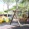 Area giochi con altalena di legno e struttura colorata in parco alberato.