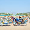 Spiaggia con lettini blu e ombrelloni arancioni, persone rilassate sotto il sole.