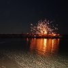 Fuochi d'artificio illuminano il cielo sopra l'acqua di notte.