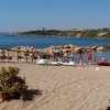 Spiaggia sabbiosa con ombrelloni colorati e pedalò. In lontananza, scogli e colline verdi.