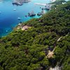 Vista aerea di una costa boscosa con mare blu e barche.