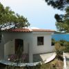 Casa bianca con terrazza coperta, pini intorno e vista sul mare.