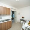 Cucina con mobili in legno, tavolo bianco con cestino di frutta, porta aperta vista mare.