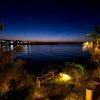 Vista notturna di una baia illuminata con cielo scuro e vegetazione in primo piano.