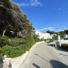 Strada in salita con case e vegetazione ai lati sotto un cielo blu.