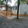 Casa mobile bianca con veranda in legno circondata da alberi.