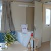 Un interno luminoso con tavolo apparecchiato, una finestra, frigo e porta aperta.