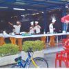 Cucinieri in divisa preparano cibo sotto una tettoia, decorata con sedie rosse e una bici.