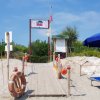 Passerella di legno conduce a una spiaggia con ombrelloni blu e sdraio.