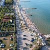 Una strada con spiaggia e mare. Ombrelloni e lettini sulla sabbia, auto parcheggiate a sinistra.