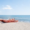 Una barca rossa sulla spiaggia di fronte al mare calmo, cielo azzurro.