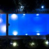 Piscina illuminata di notte, vista dall'alto, con luci che riflettono nell'acqua.