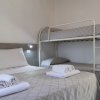 Dettaglio di un letto matrimoniale e letti a castello con lenzuola grigie e asciugamani bianchi.