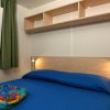 Camera con letto matrimoniale, copriletto blu, mensola e finestra con tenda verde.