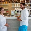 Due persone al bancone di un bar, sorridenti e vestite di bianco.
