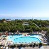 Piscina a forma di fagiolo circondata da lettini e ombrelloni, con vista sul mare e vegetazione.