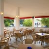 Caffetteria all'aperto con sedie e tavoli di vimini. Grandi finestre aperte con vista sugli alberi.