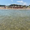 Vista del mare limpido verso una spiaggia affollata con ombrelloni e gente.