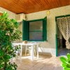 Terrazza con tavolo bianco e sedie, circondata da piante verdi e ingresso con porta a tende.