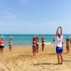Persone fanno esercizi sulla spiaggia, rivolte verso il mare.