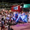 Un gruppo di persone in scena con abiti colorati e decorazioni luminose.