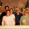 Sei persone sorridenti davanti a un bancone con bottiglie sullo sfondo.