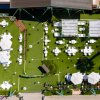 Cortile con tavoli bianchi e pergolati su prato verde.