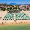 Vista dall'alto di una spiaggia affollata con ombrelloni verdi e bagnanti in acqua.