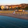 Vista aerea di una spiaggia con ombrelloni gialli, edifici e colline sullo sfondo.