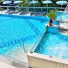 Piscina azzurra con ombrelloni a righe blu e bianche, vasca idromassaggio e piante in vaso.