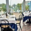 Interno di un ristorante con tavoli apparecchiati e grandi finestre che mostrano palme esterne.