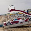 Un pedalò a forma di auto è arenato su una spiaggia con ombrelloni gialli e blu.